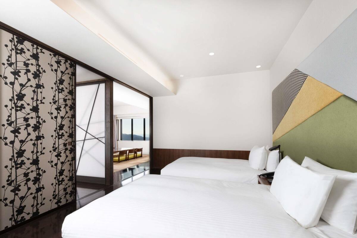 Una habitación de hotel moderna con una cama grande, vistas a través de una puerta corredera y un diseño geométrico en la pared.