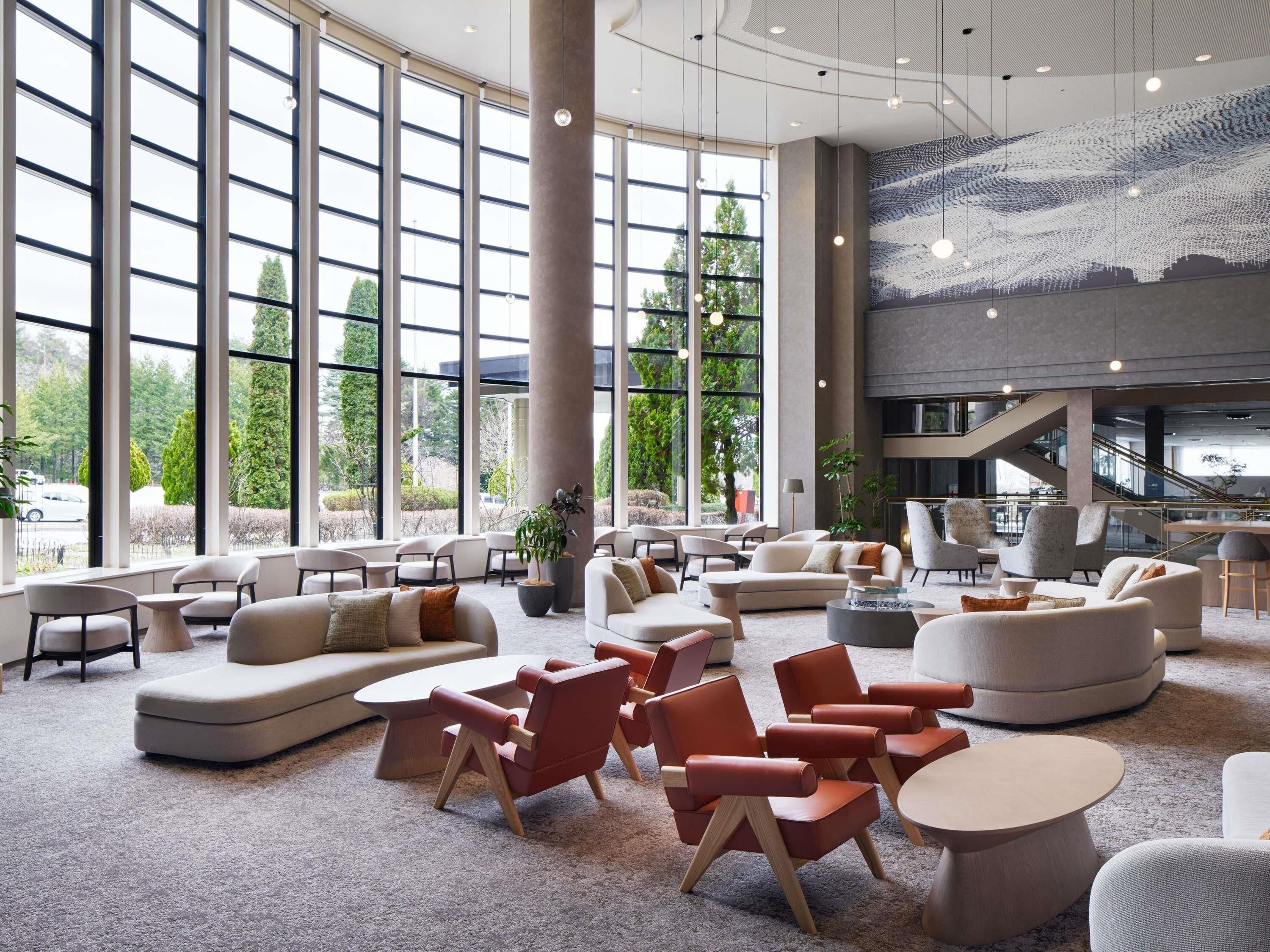 A spacious lobby with large windows, multiple seating areas, and a staircase leading to an upper level.