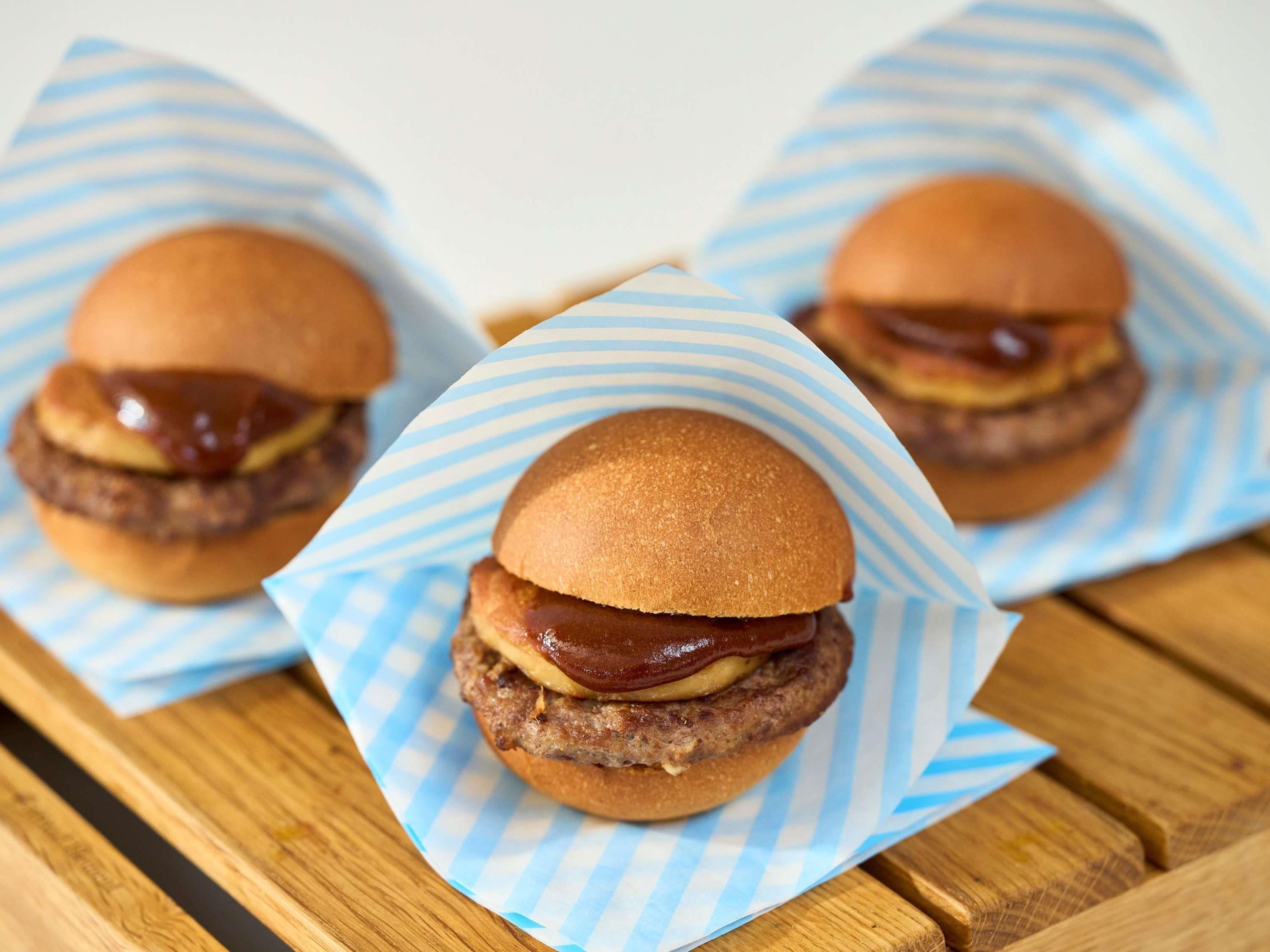 Three burgers on a wooden table with blue and white striped paper.