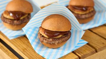 Three burgers on a wooden table with blue and white striped paper.