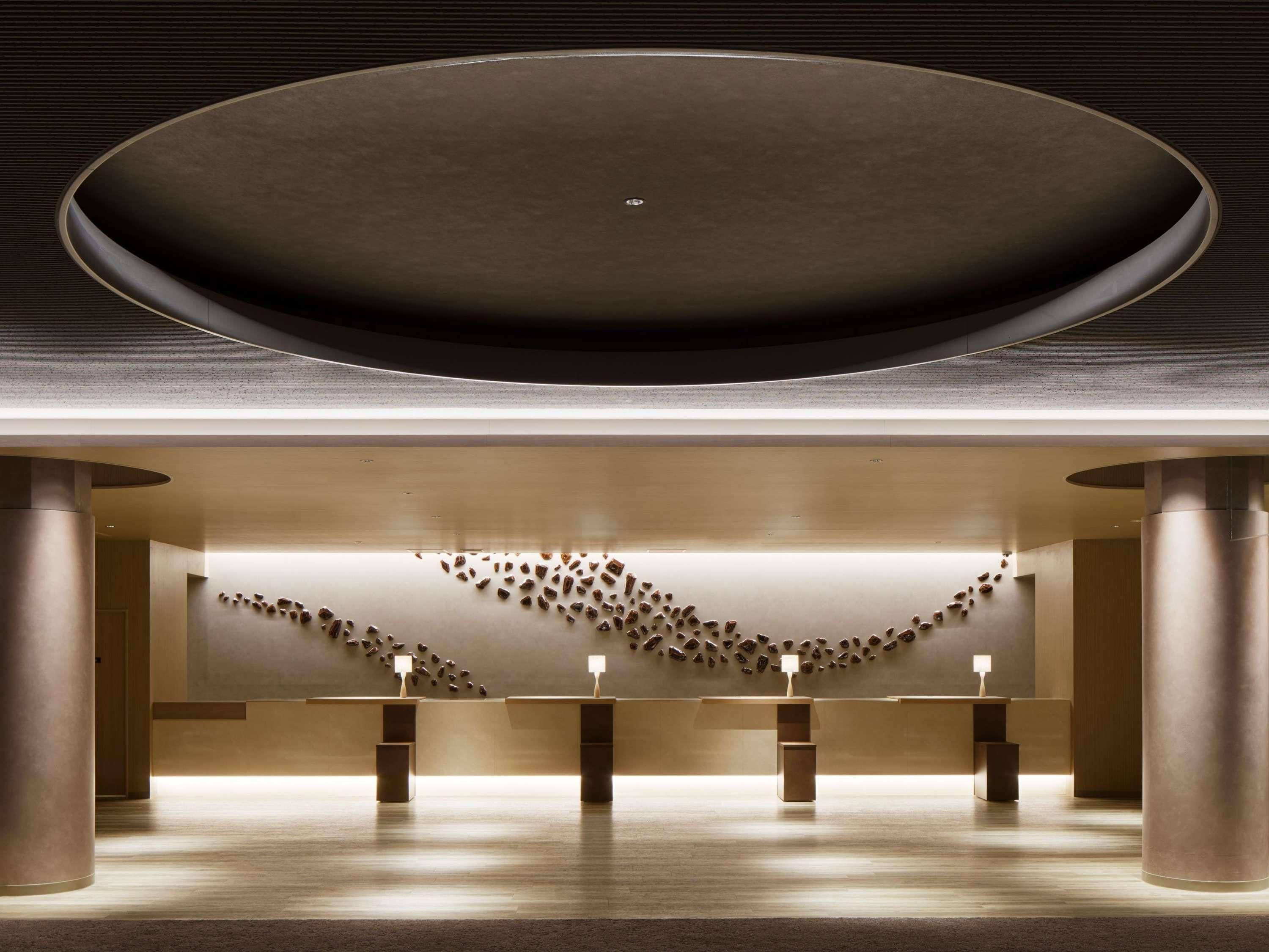 A modern interior with a central circular ceiling, a reception desk, and a wall with scattered objects.