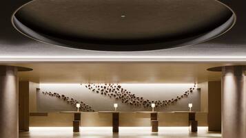 A modern interior with a central circular ceiling, a reception desk, and a wall with scattered objects.