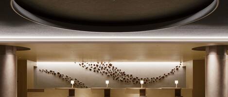 A modern interior with a central circular ceiling, a reception desk, and a wall with scattered objects.