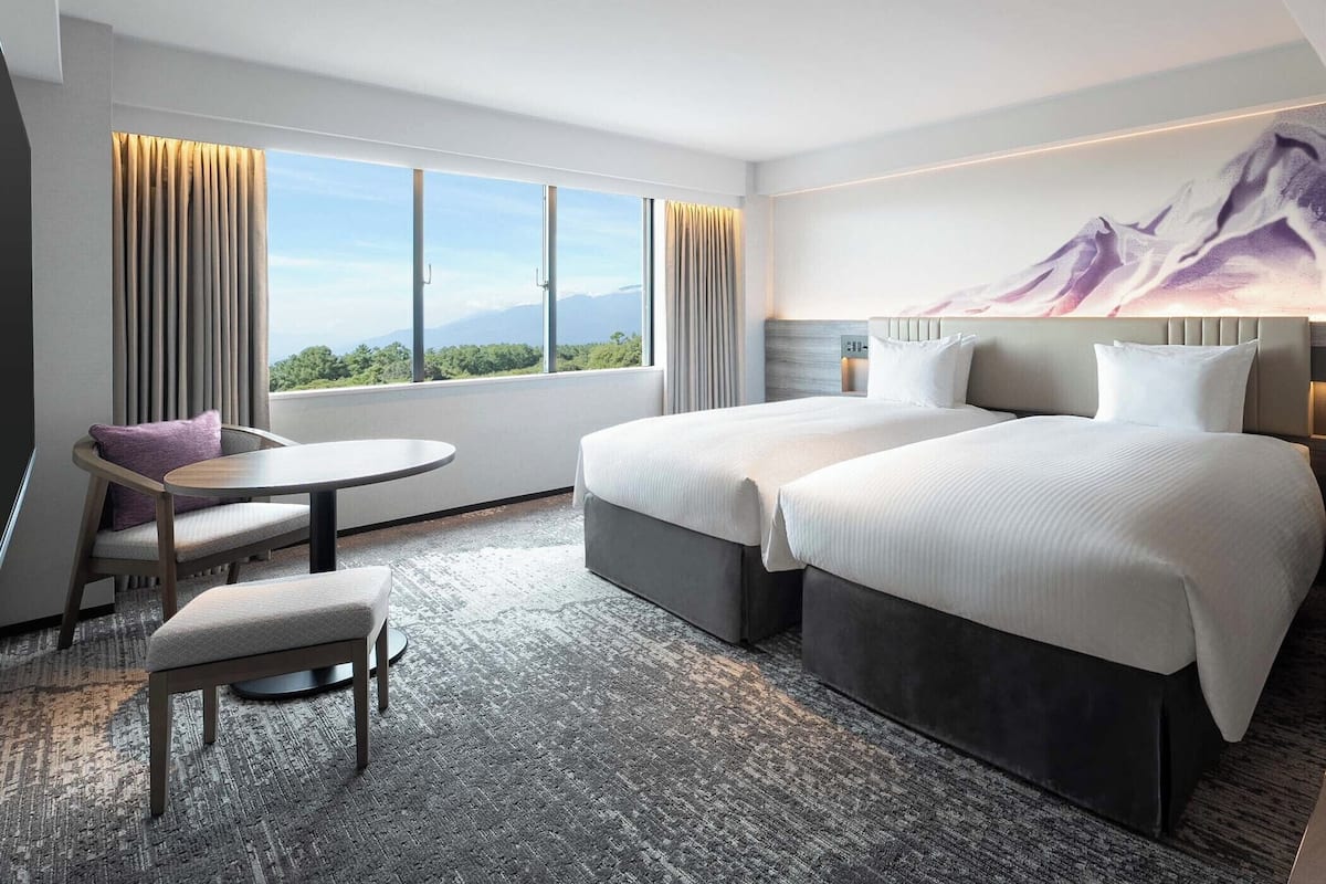 A modern hotel room with two beds, a desk, and a chair.