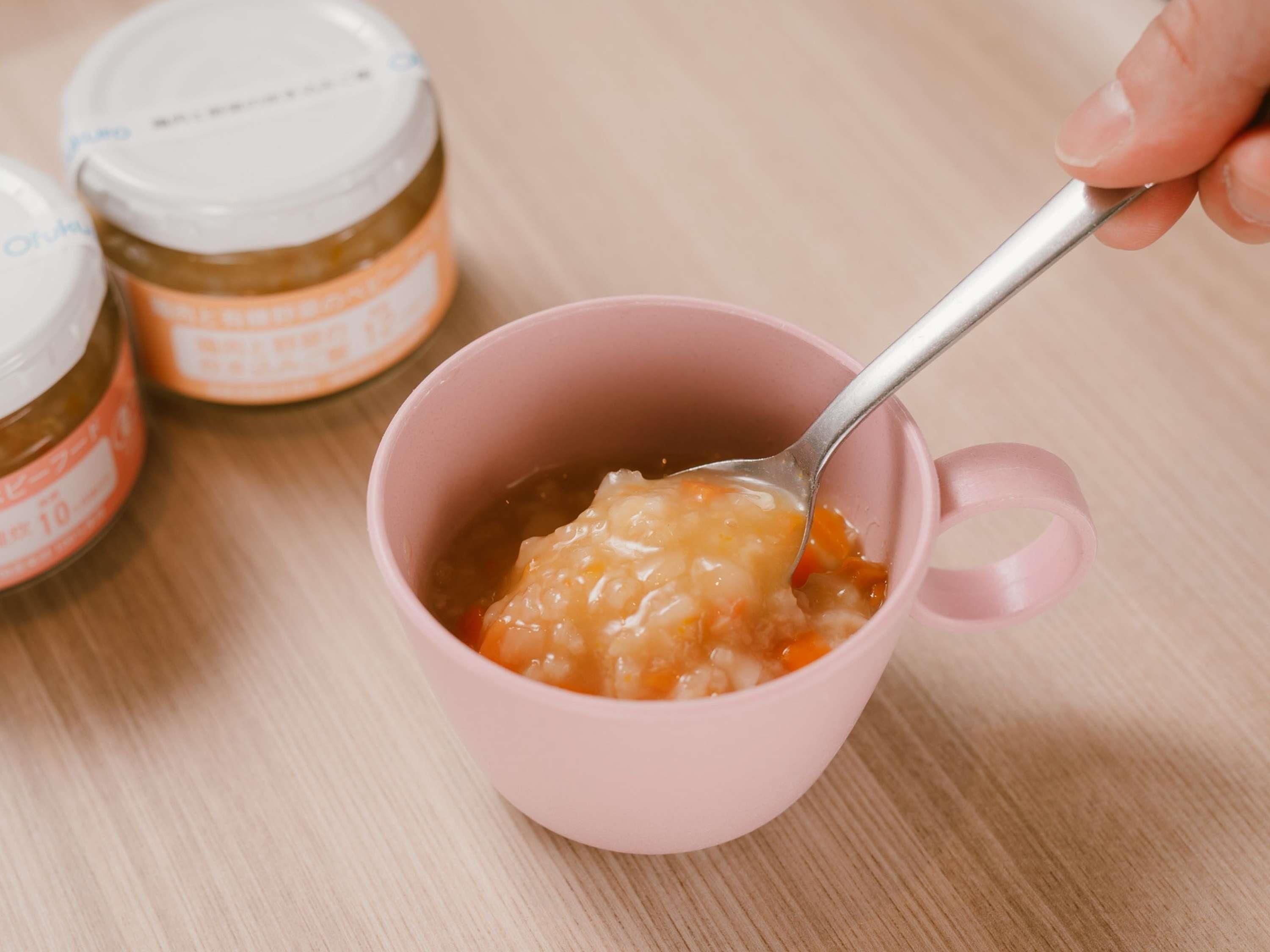 Une tasse rose contenant une cuillère de nourriture, et deux bocaux en arrière-plan.