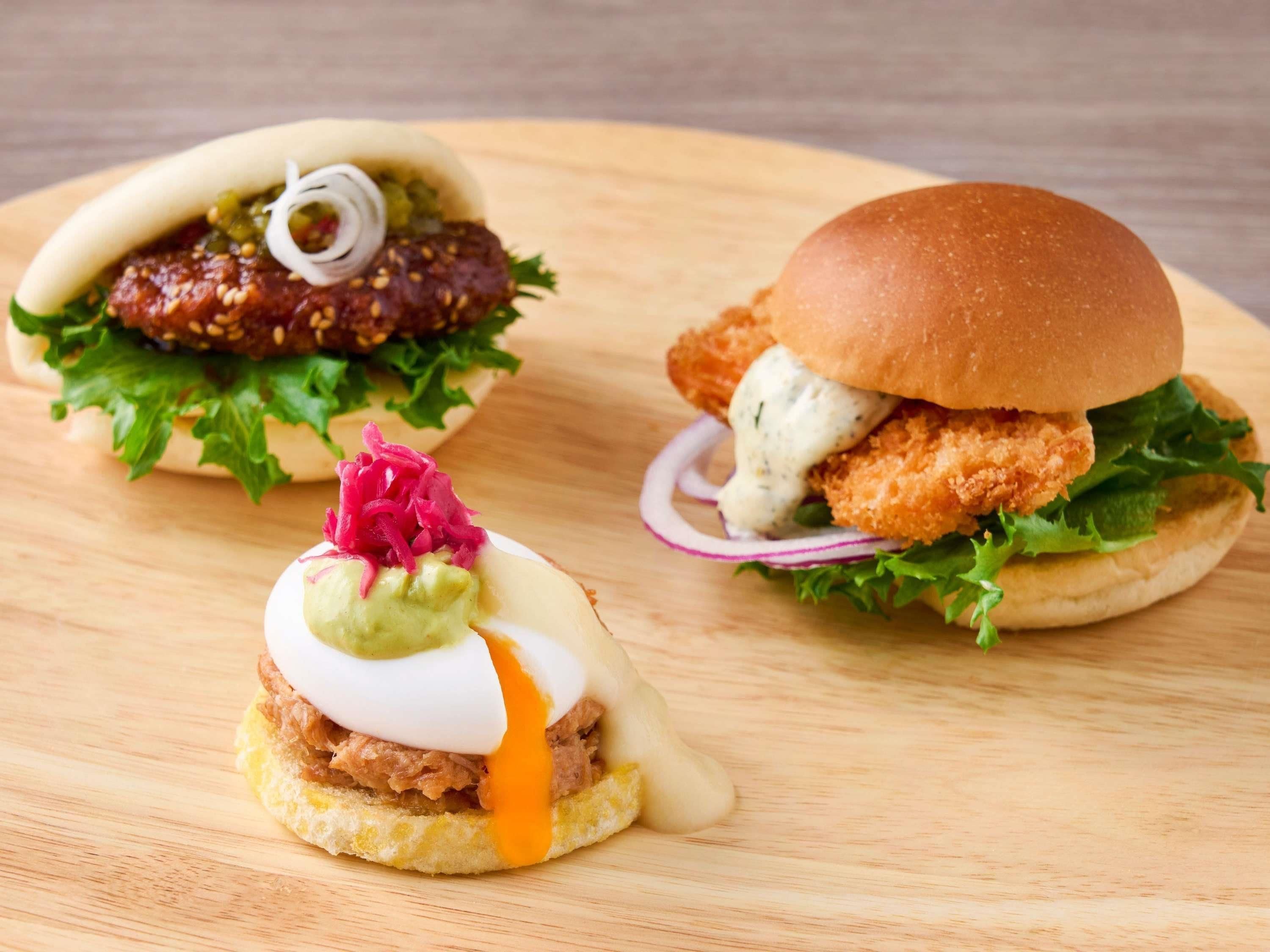 Three burgers on a wooden board.