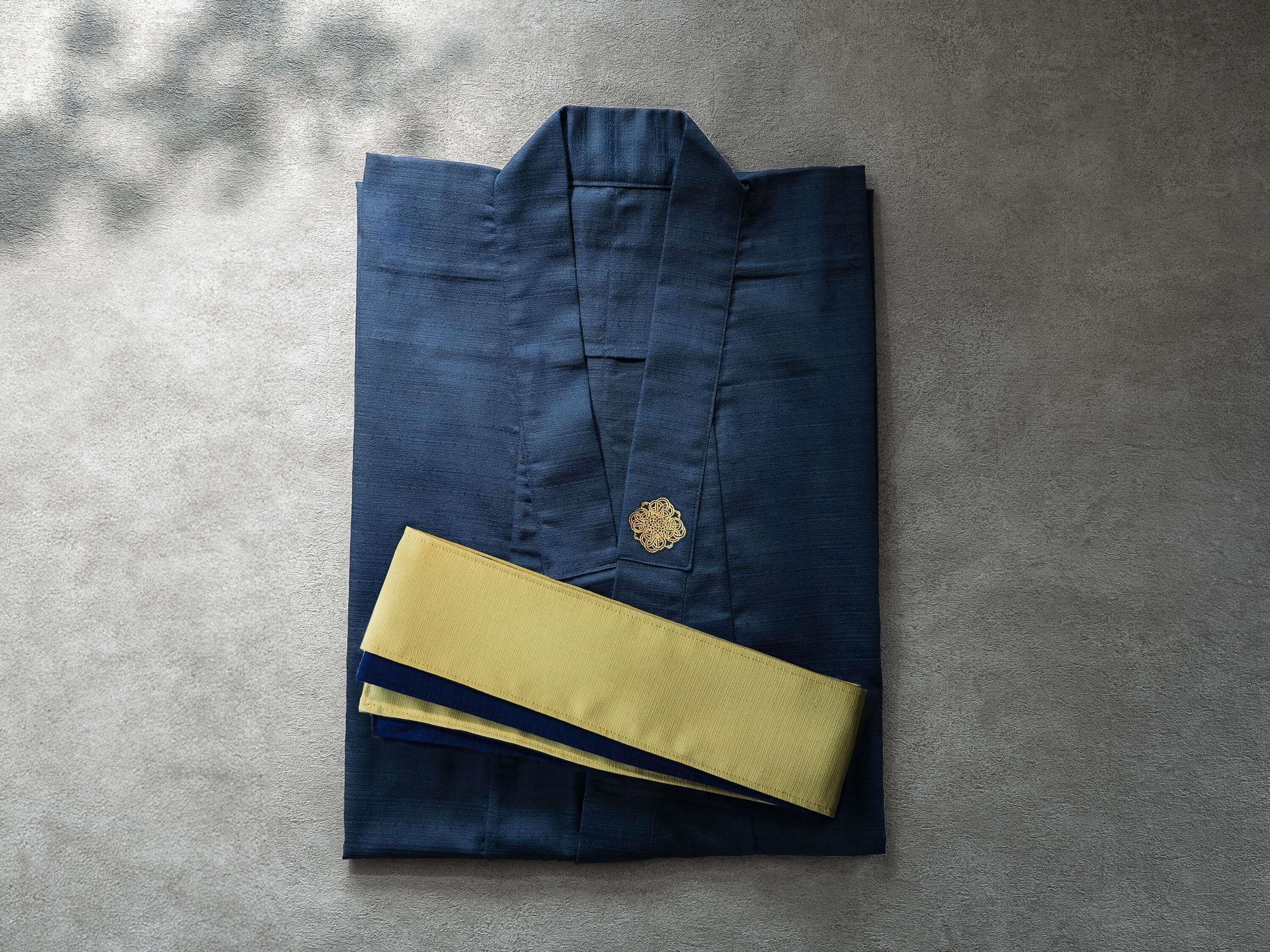 A neatly folded dark blue shirt with a gold emblem and a yellow cufflink on a textured surface.