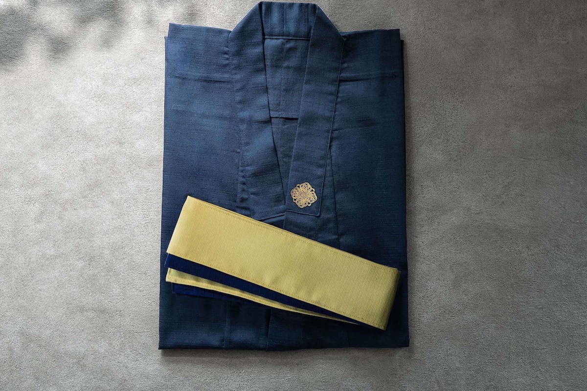 A neatly folded dark blue shirt with a gold emblem and a yellow cufflink on a textured surface.