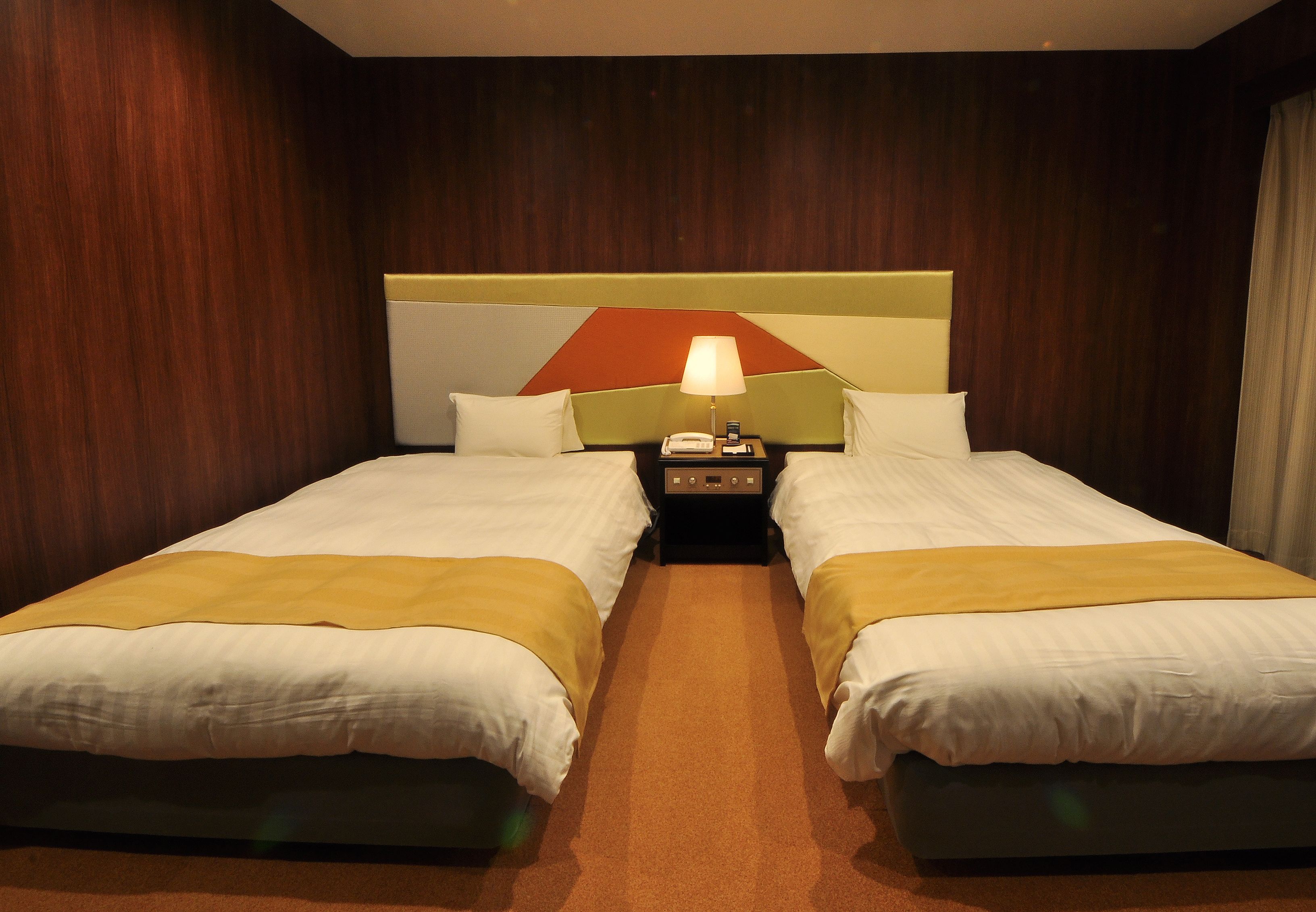 Une chambre d’hôtel avec deux lits, une table de chevet avec une lampe et un mur orné d’un motif géométrique.