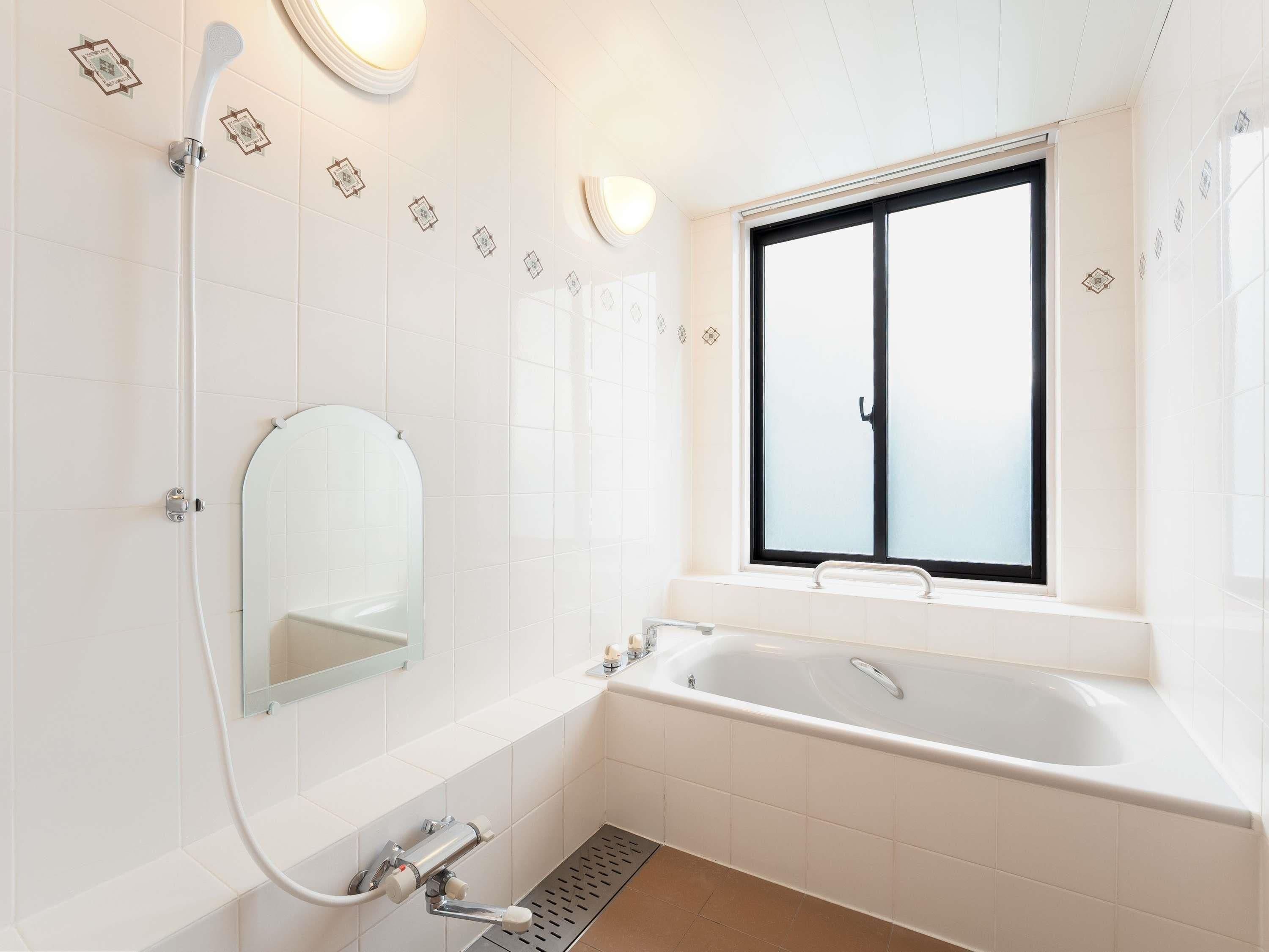 Ein modernes Badezimmer mit Badewanne, Dusche, Fenster und Spiegel.