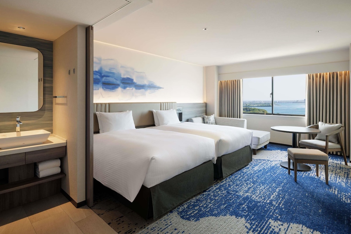 Een hotelkamer met een groot bed, een bureau, een stoel en uitzicht op de stad.