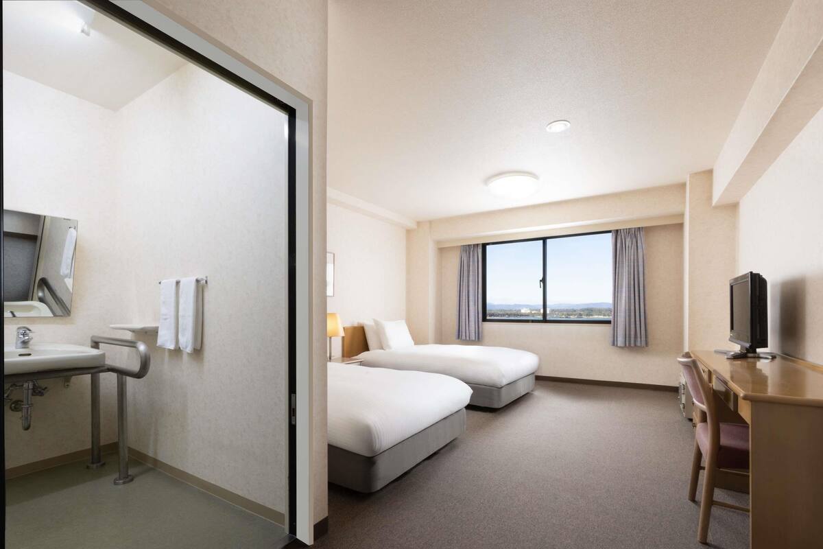 A hotel room with a bed, a desk, a TV, and a bathroom with a sink and mirror.