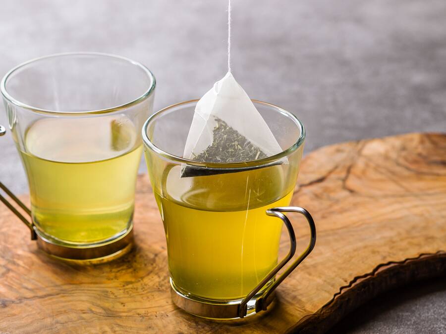 Two glass cups with handles, each containing a yellow liquid, on a wooden tray.