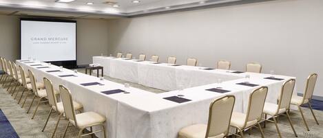 A conference room with a long table, chairs, a projector screen, and a carpeted floor.