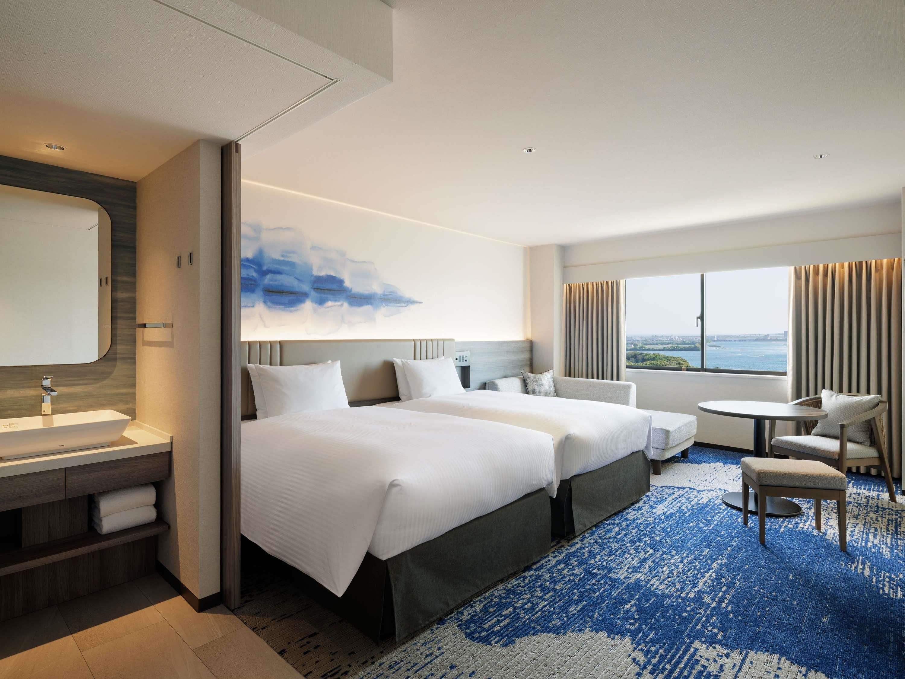 Een hotelkamer met een groot bed, een bureau, een stoel en uitzicht op de stad.