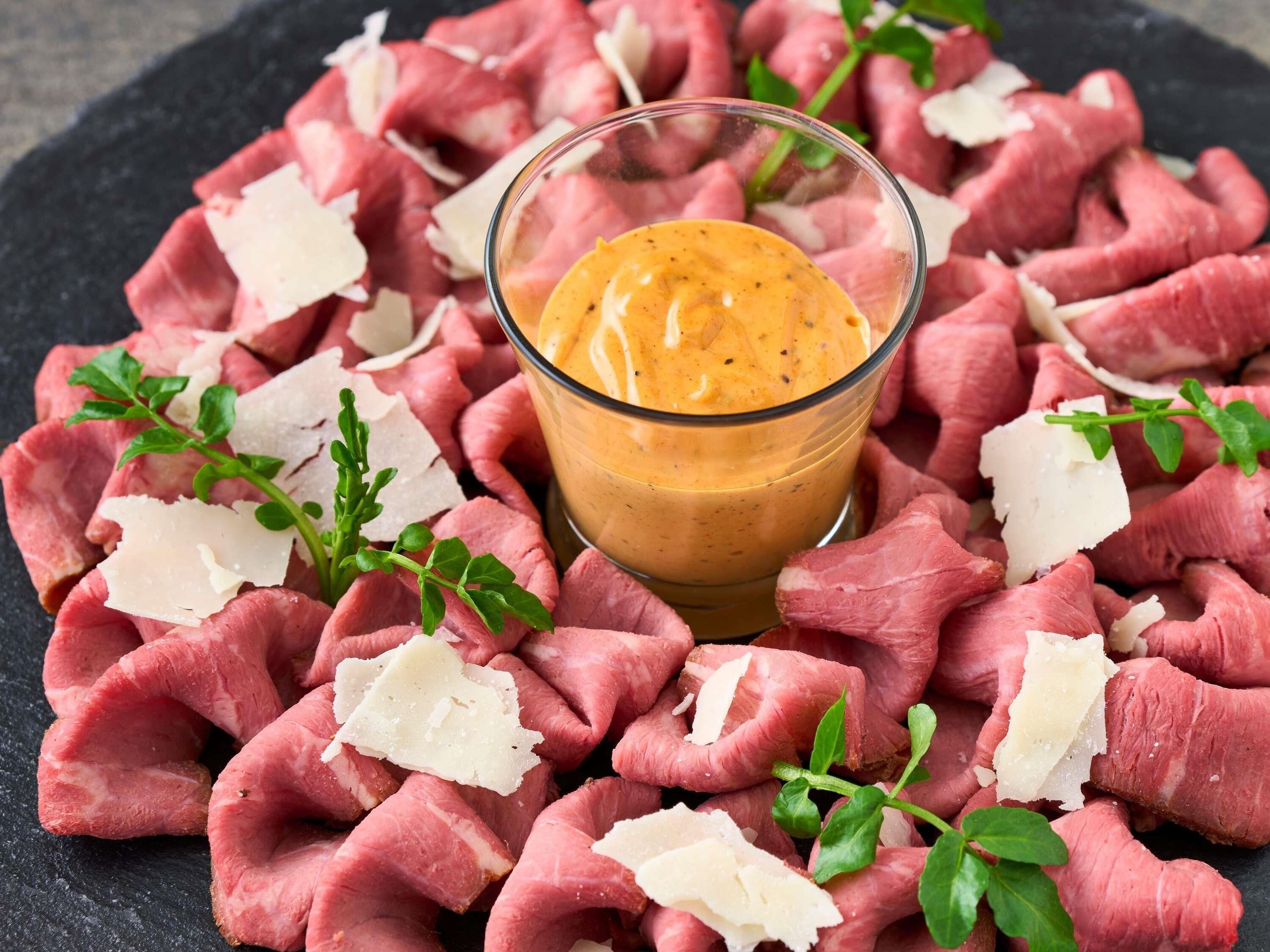 Raw meat, grated cheese, and a dipping sauce on a dark surface.