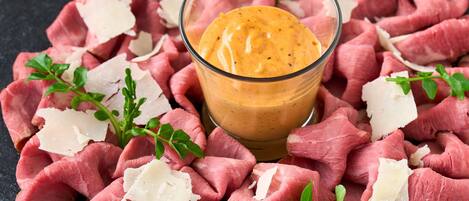 Raw meat, grated cheese, and a dipping sauce on a dark surface.