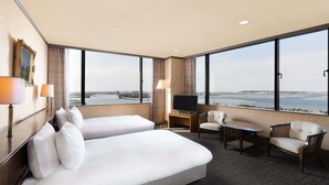 Quarto de hotel com duas camas, televisão, escrivaninha e vista para a água.