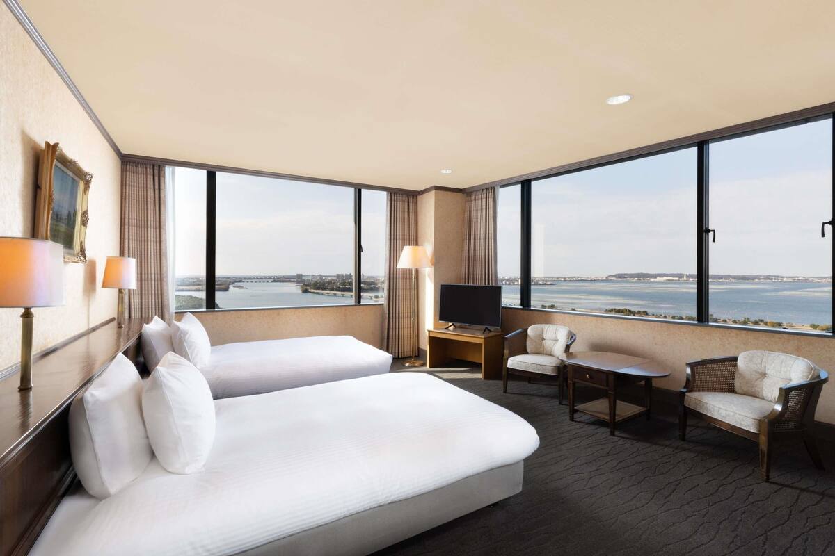 Habitación de hotel con dos camas, televisión, escritorio y vista al agua.