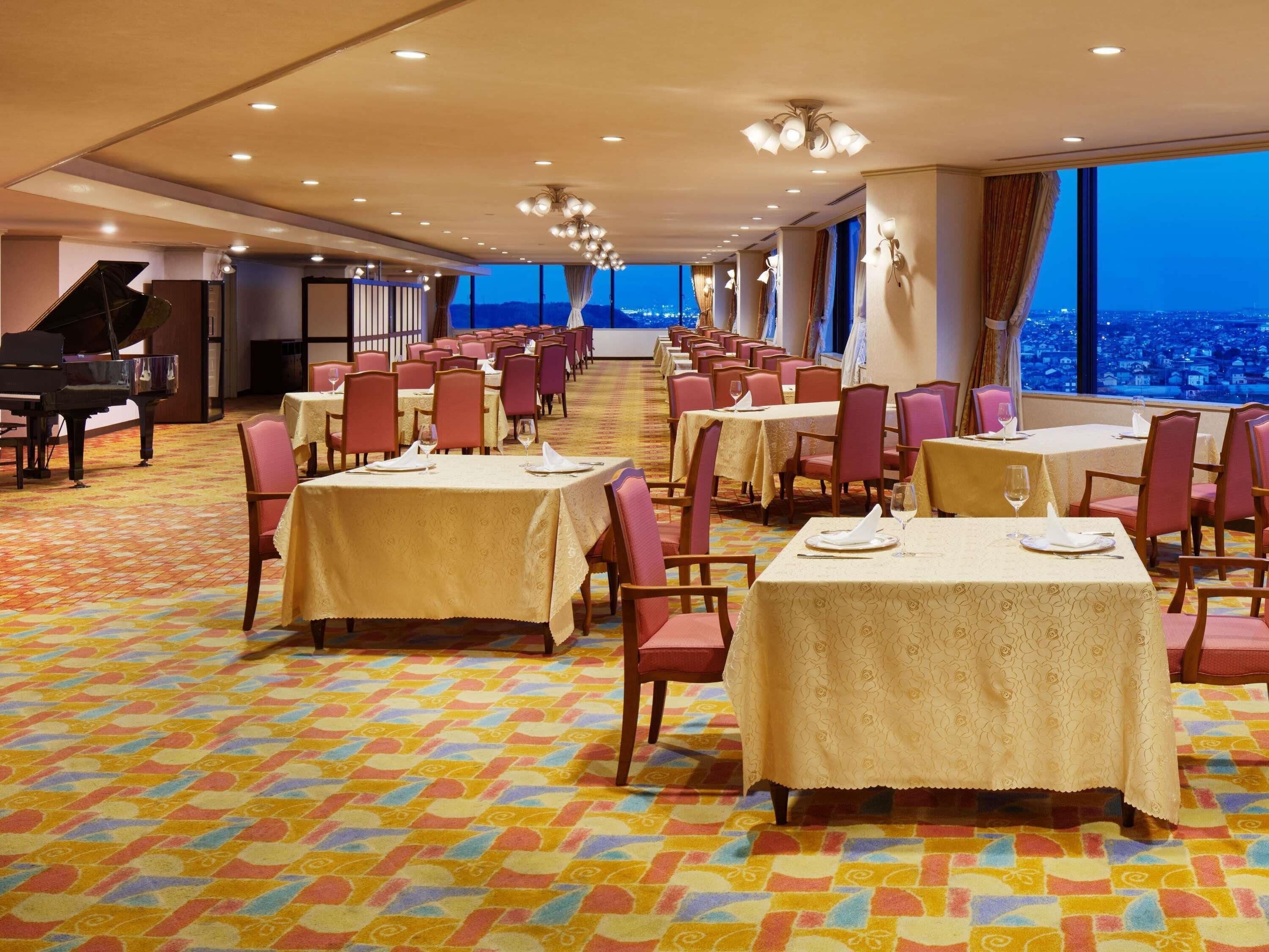 A hotel dining area with tables set for guests, a grand piano, and a city view.