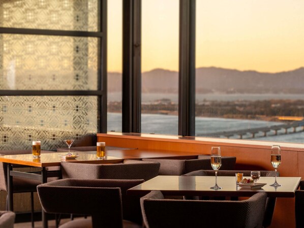 A restaurant with tables and chairs, a view of a bridge, and a cityscape in the background. - Grand Mercure Lake Hamana Resort & Spa (Hamamatsu)