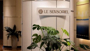 Uma receção com uma placa a dizer "LE SENSORIEL" e uma planta em vaso em primeiro plano.