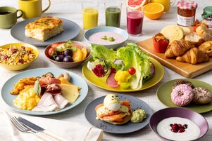 Una mesa de desayuno con distintos platos, como huevos, tostadas y bollería.