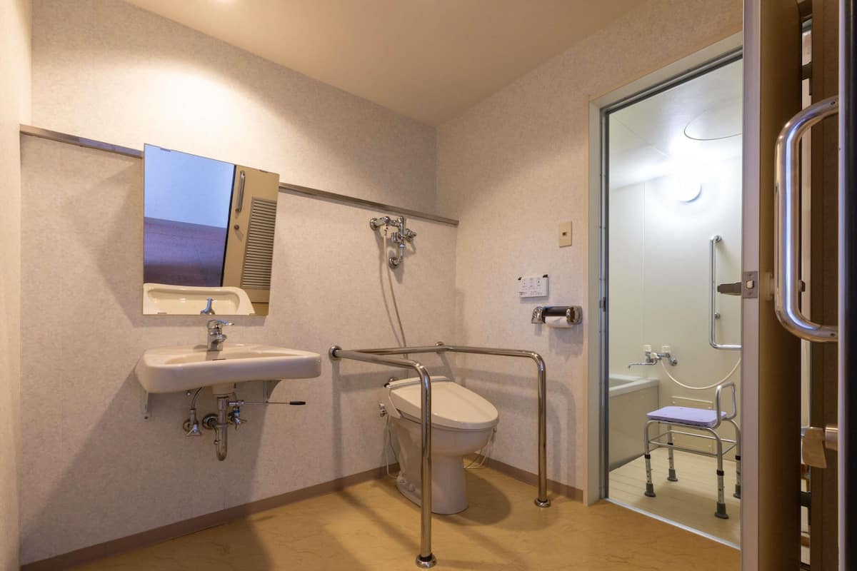 Une salle de bain équipée d’un lavabo, de toilettes et d’une douche, avec des barres d’appui et une douche accessible aux personnes en fauteuil roulant.