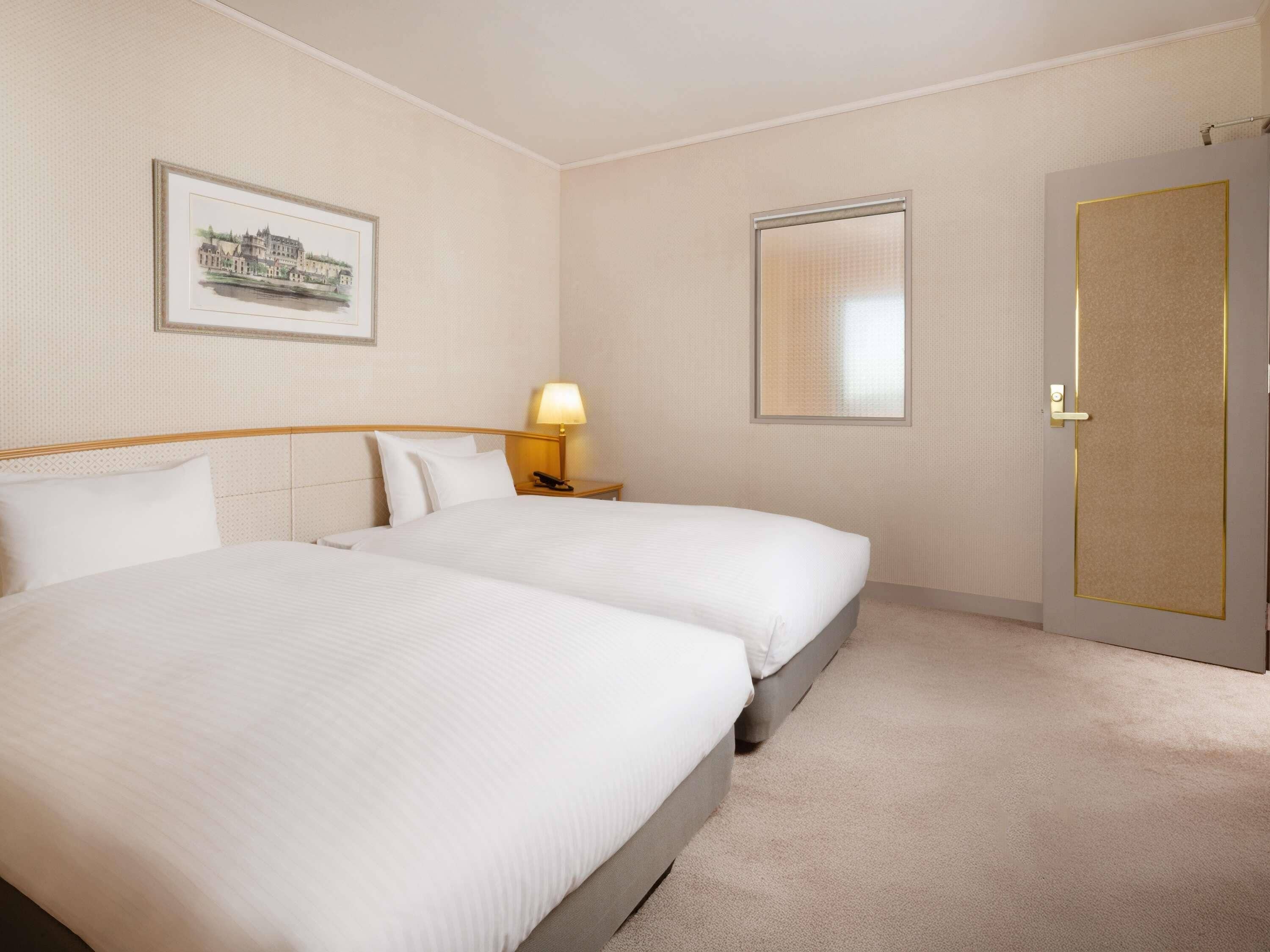 Une chambre d’hôtel avec deux lits, une table de chevet avec une lampe, un tableau encadré au mur et une porte avec un cadre doré.