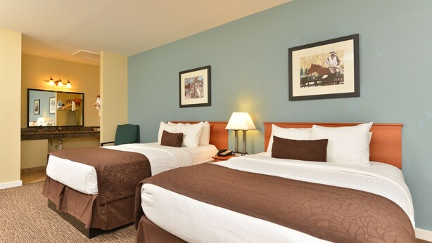A hotel room with two beds, a bathroom with a mirror, and two framed pictures on the wall. - The Texas Lodge (Gonzales)