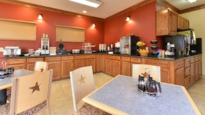 A hotel dining area with wooden cabinets, a buffet counter, and a table with chairs. - The Texas Lodge (Gonzales)
