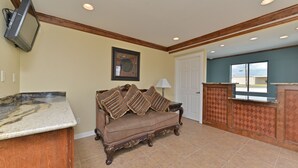 A living room with a sofa, a television mounted on the wall, and a door leading to another room. - The Texas Lodge (Gonzales)