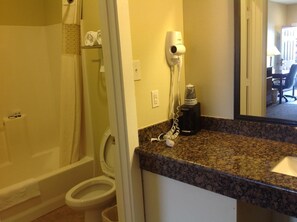 A bathroom with a toilet, a shower, a hairdryer, and a coffee maker on the counter. - The Texas Lodge (Gonzales)