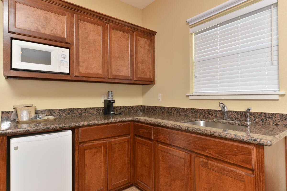 A kitchen with wooden cabinets, a microwave, a coffee maker, and a window with blinds.