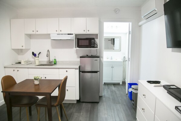 A compact kitchen with white cabinets, a stainless steel refrigerator, a microwave, and a dining area with a table and chairs. - Westview Centre Motel Ltd. (Powell River)