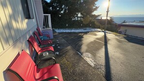 A parking area with red chairs and a table, a building with a white exterior, and a view of the ocean with the sun setting in the background. - Westview Centre Motel Ltd. (Powell River)