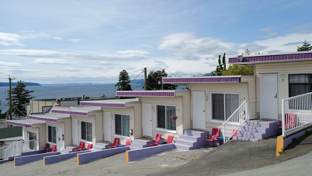 A row of small, single-story cabins with a view of the sea. Each cabin has a porch with a few chairs and a small table. - Westview Centre Motel Ltd. (Powell River)