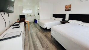 A hotel room with two beds, a desk with a chair, a television mounted on the wall, and a small kitchenette in the background. - Westview Centre Motel Ltd. (Powell River)