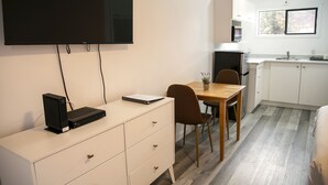 A modern kitchen with white cabinets, a wooden dining table, and a flat-screen TV mounted on the wall. - Westview Centre Motel Ltd. (Powell River)