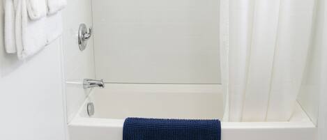 A modern bathroom with a walk-in shower, white tiles, a blue towel, and a gold shower curtain rod.