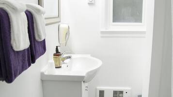 Une petite salle de bain avec un lavabo blanc, un miroir, une fenêtre et un porte-serviettes avec des serviettes violettes.