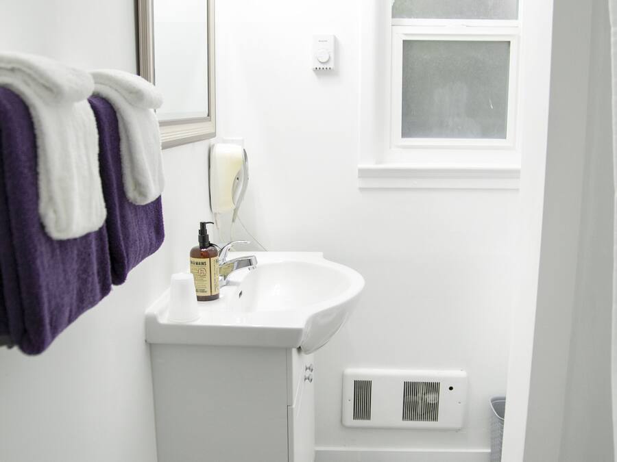Une petite salle de bain avec un lavabo blanc, un miroir, une fenêtre et un porte-serviettes avec des serviettes violettes.