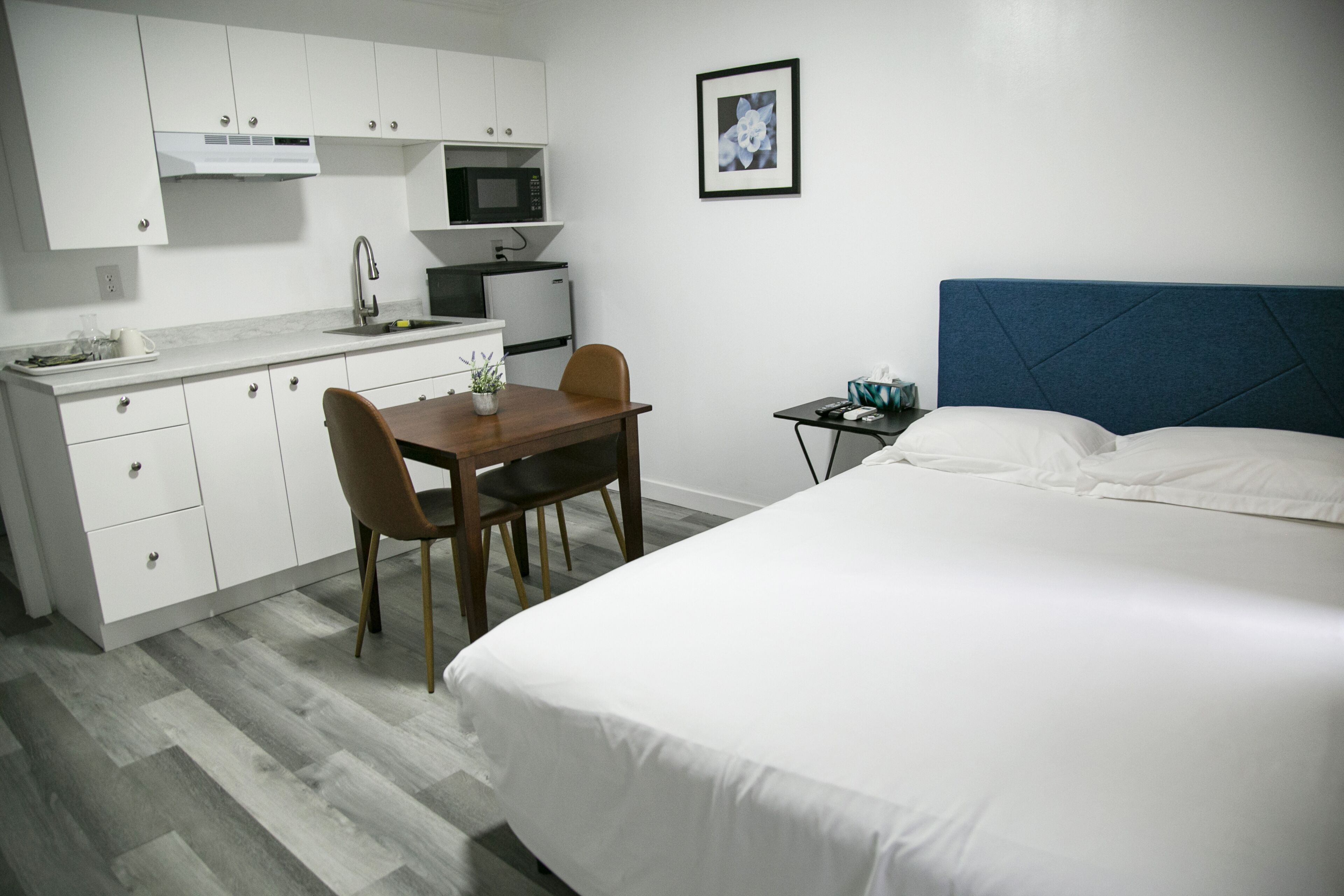 A hotel room with a bed, a small desk, a chair, a microwave, a sink, and a cabinet.