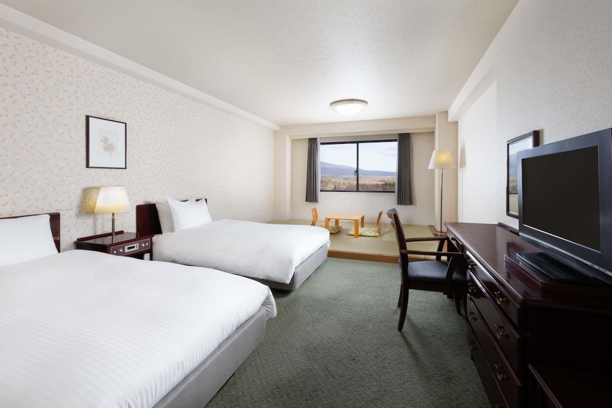 A hotel room with two beds, a desk with a chair, a television, and a window with a view.