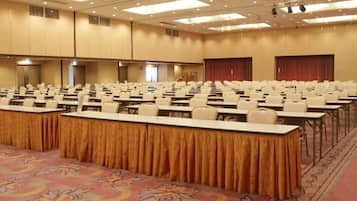 A large conference room with rows of tables and chairs, carpeted floor, and a stage area.