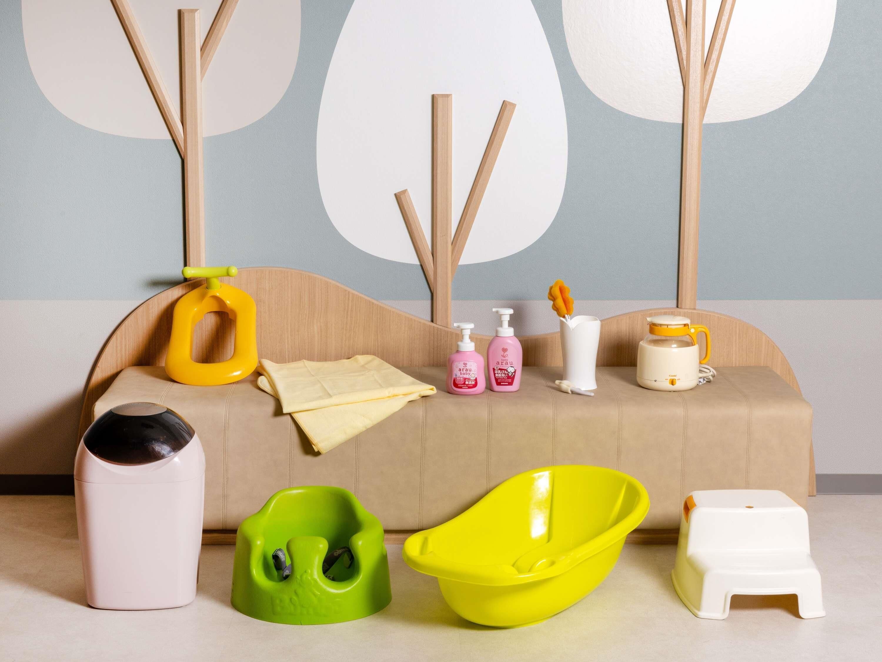 A room with a beige sofa, a yellow toy, a green and a yellow bath tub, a white trash bin, and a white stool.