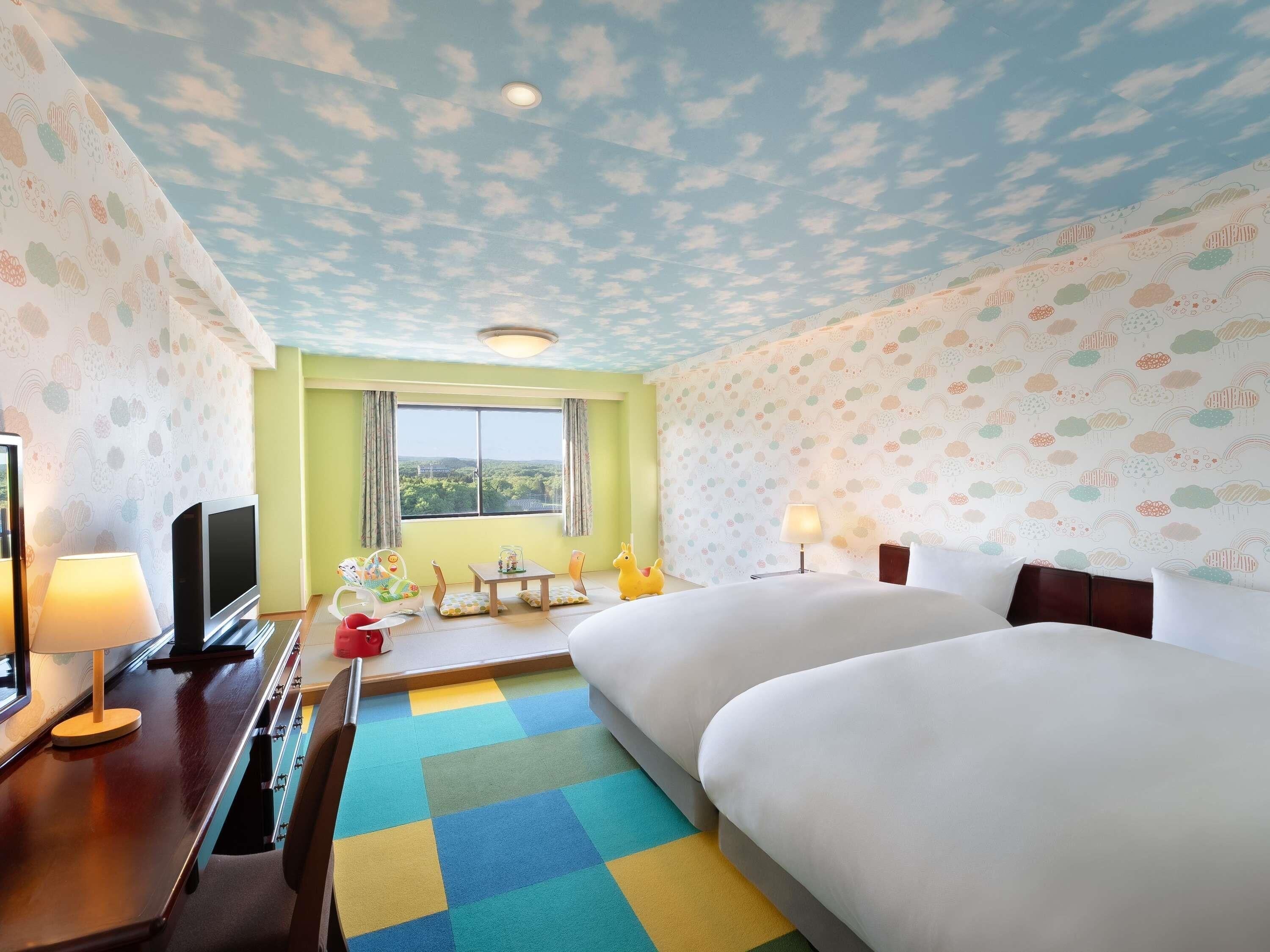 A hotel room with a large bed, a desk with a TV, a window with a view, and a colorful ceiling.