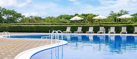 A swimming pool with lounge chairs and umbrellas, surrounded by neatly trimmed hedges and trees.