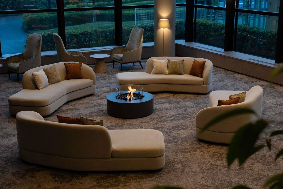 A modern lounge area with sofas and a central coffee table, large windows with a view of a landscaped garden.