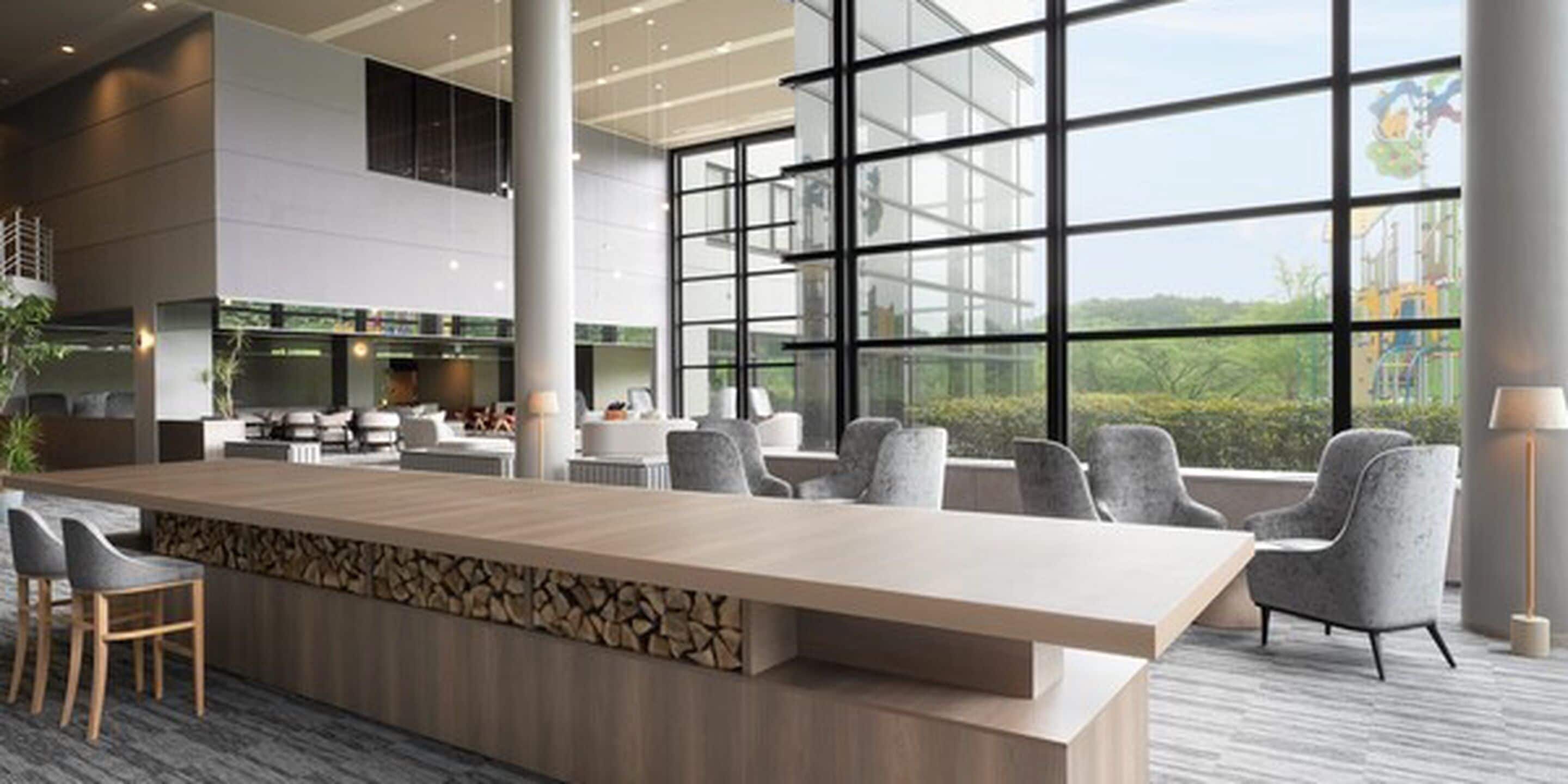 Un hall d’hôtel moderne avec un long comptoir d’accueil, des sièges confortables et de grandes fenêtres donnant sur l’extérieur.